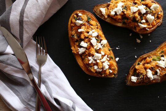 Top view of sweet potaoes with feta cheese on a black surface with a cloth and silverware