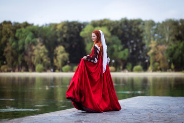 Portrait of a red-haired woman in a historical costume of the 15th century - a red slit dress in...