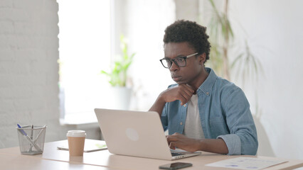 Young African Man Thinking while Working on Laptop in Office