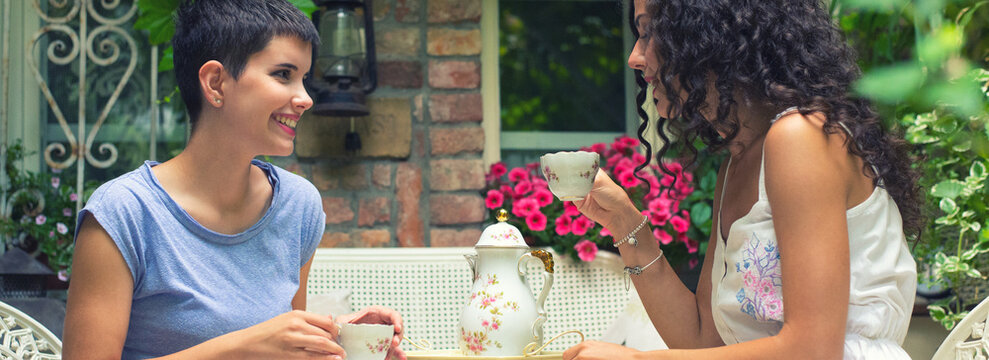 Two young smiling women drinking coffee and talking in the garden in spring 