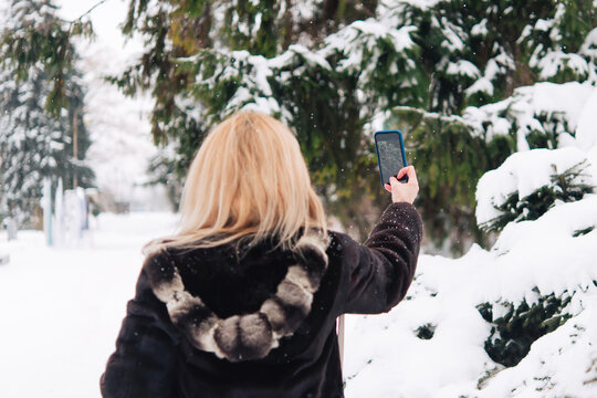 Winter landscape, Christmas trees in the snow. woman with mobile phone is photographed and shows the surrounding nature.