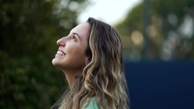 Happy hopeful young millennial woman standing outside smiling looking at sky with FAITH