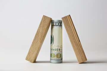 Rolled up 100 dollar bill covered with wooden cubes on a light background. Currency concept