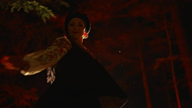 Dancing woman in traditional ukrainian handkerchief and costume on dark night forest background. Lady in vintage national dress - vyshyvanka, ancient coral beads. Concept of ethnic style.