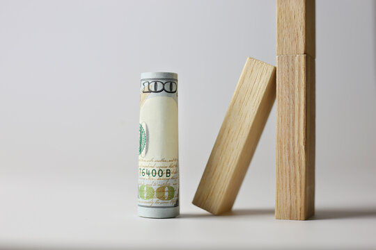 A rolled up 100 dollar bill stands next to wooden cubes on a light background. Currency concept