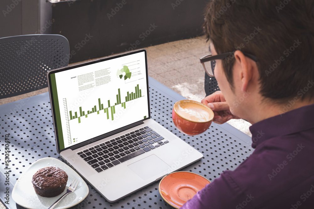 Sticker Asian businessman at table in cafe using laptop with charts and data on screen