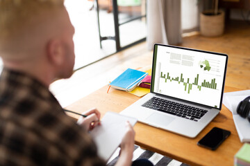 Albino african american man at table using laptop with green graphs and data on screen
