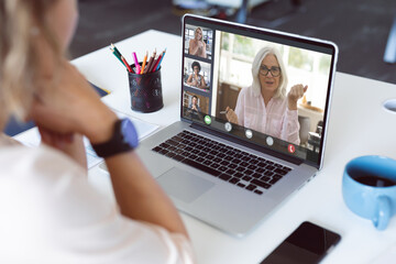 Caucasian businesswoman at desk making laptop video call with diverse colleagues on screen