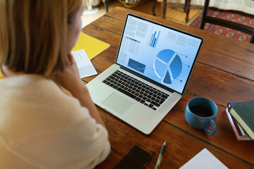 Asian businesswoman at table using laptop with charts and data on screen