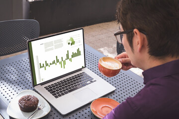 Aziatische zakenman aan tafel in café met laptop met grafieken en gegevens op het scherm