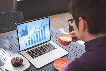Aziatische zakenman aan tafel in café met laptop met blauwe grafieken op het scherm