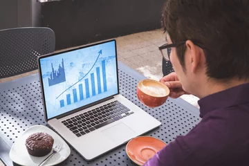 Keuken foto achterwand Aziatische plekken Aziatische zakenman aan tafel in café met laptop met blauwe grafieken op het scherm