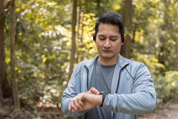 Close up man using smart watch to monitor performance, setting up his smart watch before exercise on path forest.