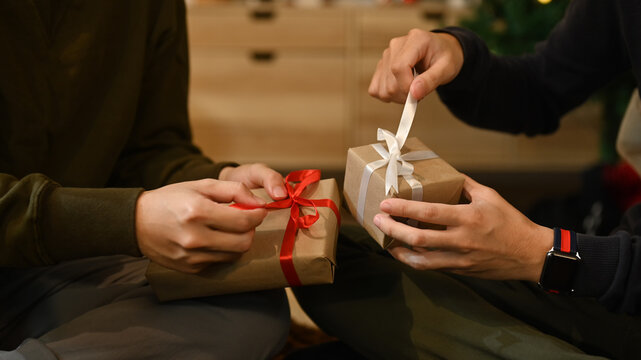 Cropped image of men celebrating Christmas, New Year at home together and exchange presents. Holidays and celebration concept