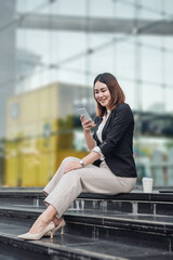 Young Asian businesswoman talking on phone and sitting in airport before business trip. Beautiful woman passenger has mobile call and discusses something with smile, holds coffee in hand