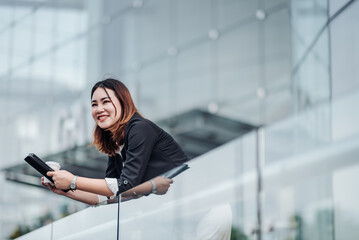 Young Asian businesswoman using tablet and sitting in airport before business trip. Beautiful woman passenger has mobile call and discusses something with smile, holds coffee in hand