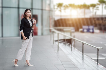 Young Asian businesswoman using tablet in airport before business trip. Beautiful woman passenger has mobile call and discusses something with smile, holds coffee in hand