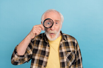 Photo of impressed funky man pensioner dressed checkered shirt looking enlarging glass isolated blue color background