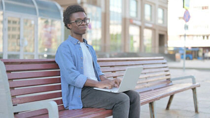 Rejecting Young African Man in Denial While using Laptop Sitting Outdoor on Bench