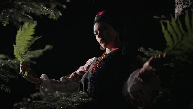 Authentic woman dancing with ferns on night forest background.i Witch in traditional ukrainian handkerchief, necklace and costume. Lady in national dress - vyshyvanka, ancient coral beads.