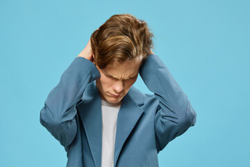 a young man in a classic suit covers his ears with his hands and frowns his face, lowering it down