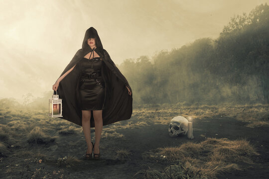 Asian witch woman with a black cloak holding a lantern standing