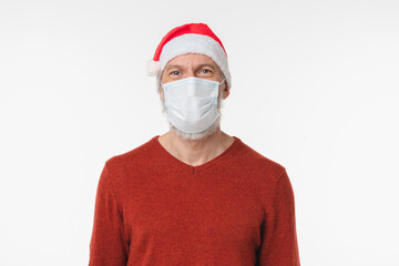 Grey-haired man in red Santa Claus hat wearing protective face mask against coronavirus Covid 19 isolated in white background. Pandemic Christmas New Year concept