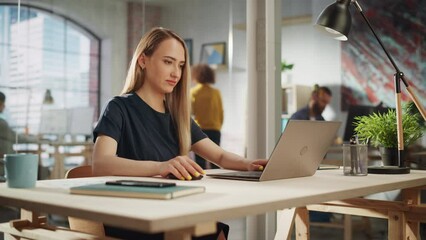 Beautiful Female in a Black Casual Dress Sitting at a Desk in Creative Office, Working on Tasks on Laptop Computer. Young Creative Specialist Writing Corporate Project Plans for Marketing Agenda.
