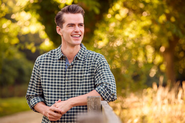 Casually Dressed Man Leaning On Fence On Walk In Countryside