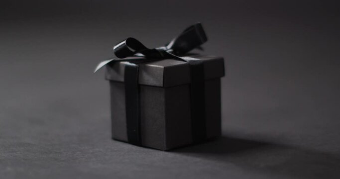 Black gift box with black ribbon on dark grey background with copy space