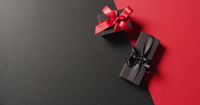 Overhead view of two black gift boxes with red and black ribbons on black and red with copy space