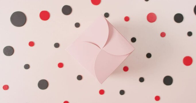 Overhead view of pink gift box on white background with red and black dots