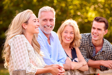 Multi-Generation Family With Adult Offspring Leaning On Fence Walking In Countryside