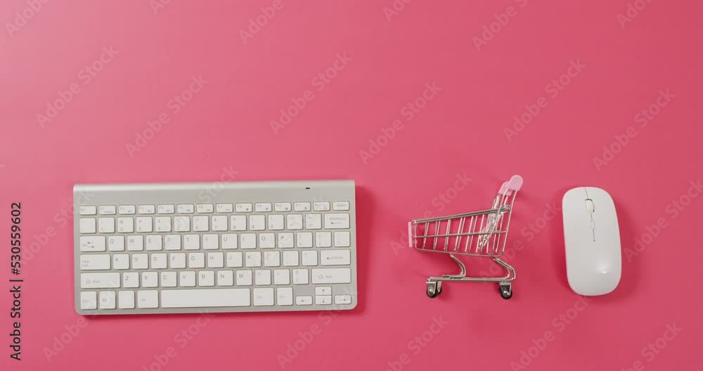 Poster overhead view of computer keyboard, shopping trolley and mouse on pink background with copy space