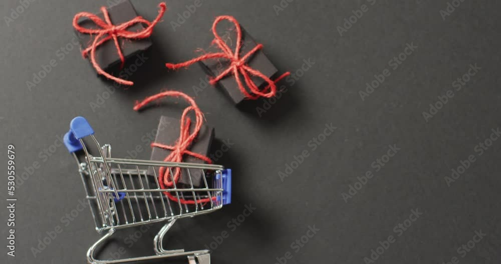 Poster three black gifts tied with red string and shopping cart on black background with copy space