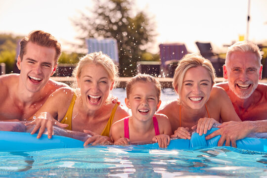 Portrait Of Smiling Multi-Generation Family On Summer Holiday Relaxing In Swimming Pool On Airbed