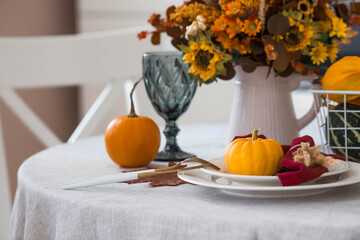 Beautiful autumn table setting. A plate with a cotton napkin and pumpkins. Table gold and a vase...