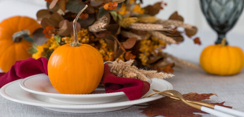Beautiful autumn table setting. A plate with a cotton napkin and pumpkins. Table gold and a vase with autumn flowers on a linen tablecloth. The concept of festive serving for Thanksgiving.