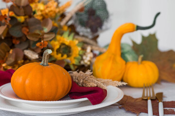 Beautiful autumn table setting. A plate with a cotton napkin and pumpkins. Table gold and a vase with autumn flowers on a linen tablecloth. The concept of festive serving for Thanksgiving.