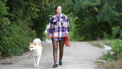Girl walks her dog Akita inu on the street on a leash. The dog and the mistress are walking along a rural road