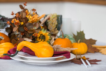 Beautiful autumn table setting. A plate with a cotton napkin and pumpkins. Table gold and a vase with autumn flowers on a linen tablecloth. The concept of festive serving for Thanksgiving.