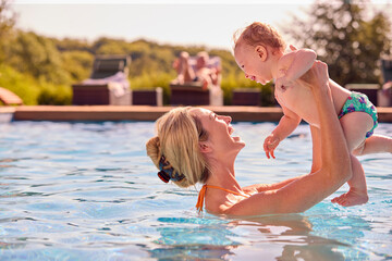 Fototapeta na wymiar Mother With Baby Son On Summer Holiday Playing In Swimming Pool