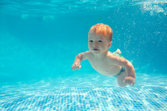 Baby Boy With Family On Summer Holiday Swimming Underwater In Pool