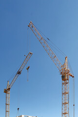 Fototapeta na wymiar Building. Construction of new houses. Construction cranes. Creation of new modern houses. Architecture. Urban landscape. Two construction cranes against the sky. Construction of a new building