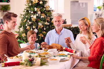 Multi-Generation Family Celebrating Christmas At Home Saying Prayer Before Eating Meal Together