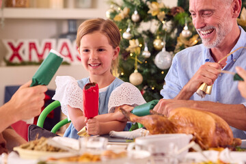 Multi-Generation Family Celebrating Christmas At Home Pulling Crackers Before Eating Meal Together