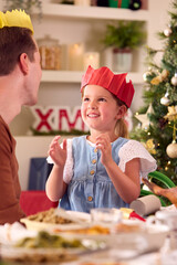 Father And Daughter Celebrate Family Christmas At Home Wearing Paper Hats Before Eating Meal