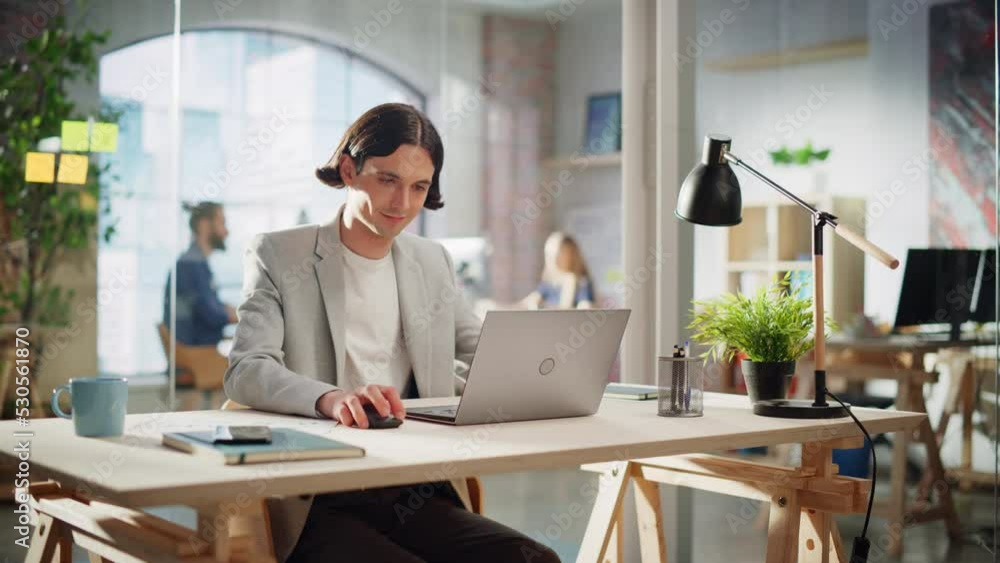 Poster happy long-haired manager sitting at a desk in creative office. young stylish man using laptop compu