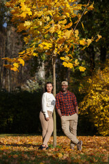 A white girl and a black guy are standing under a tree in an autumn park.