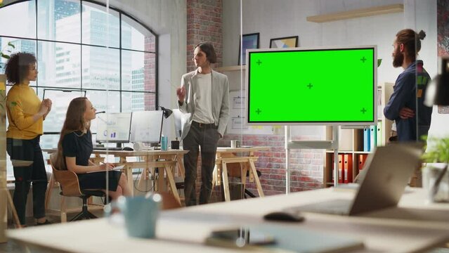 Young Businessman Leading a Team Meeting in Creative Office Conference Room. Confident Stylish Manager Showing Presentation on Green Screen Mock Up Chroma Key Monitor. Static Shot.